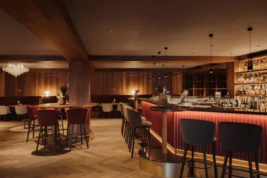 Elegantes Barinterieur mit warmem, stimmungsvollem Licht. Mit einer geschwungenen Barreihe aus gepolsterten Hockern, edlen Holzakzenten und sanfter, intimer Beleuchtung.