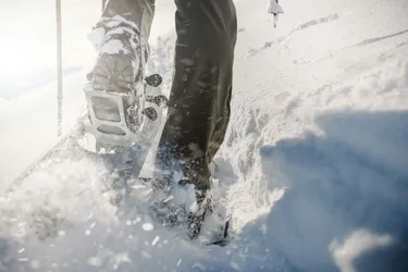 Detailaufnahme von Schneeschuhen, die im frischen Schnee während einer Winterwanderung einsinken, mit Betonung der Schneetextur und der Bewegung der Schritte.