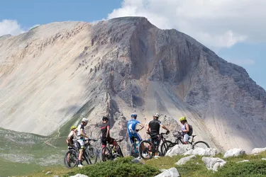 Group of cyclists taking a break on a green meadow during a dirt trail ride, watching a mountain in front of them.