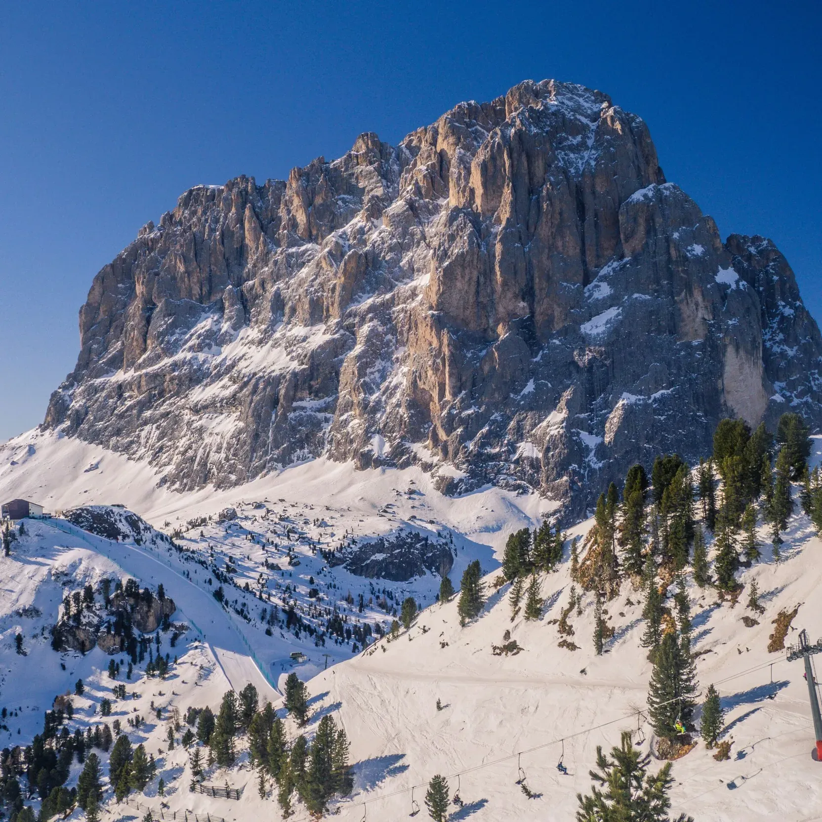 Massiccio del Sassolungo innevato in inverno, con impianto di risalita e pista da sci alle sue basi.
