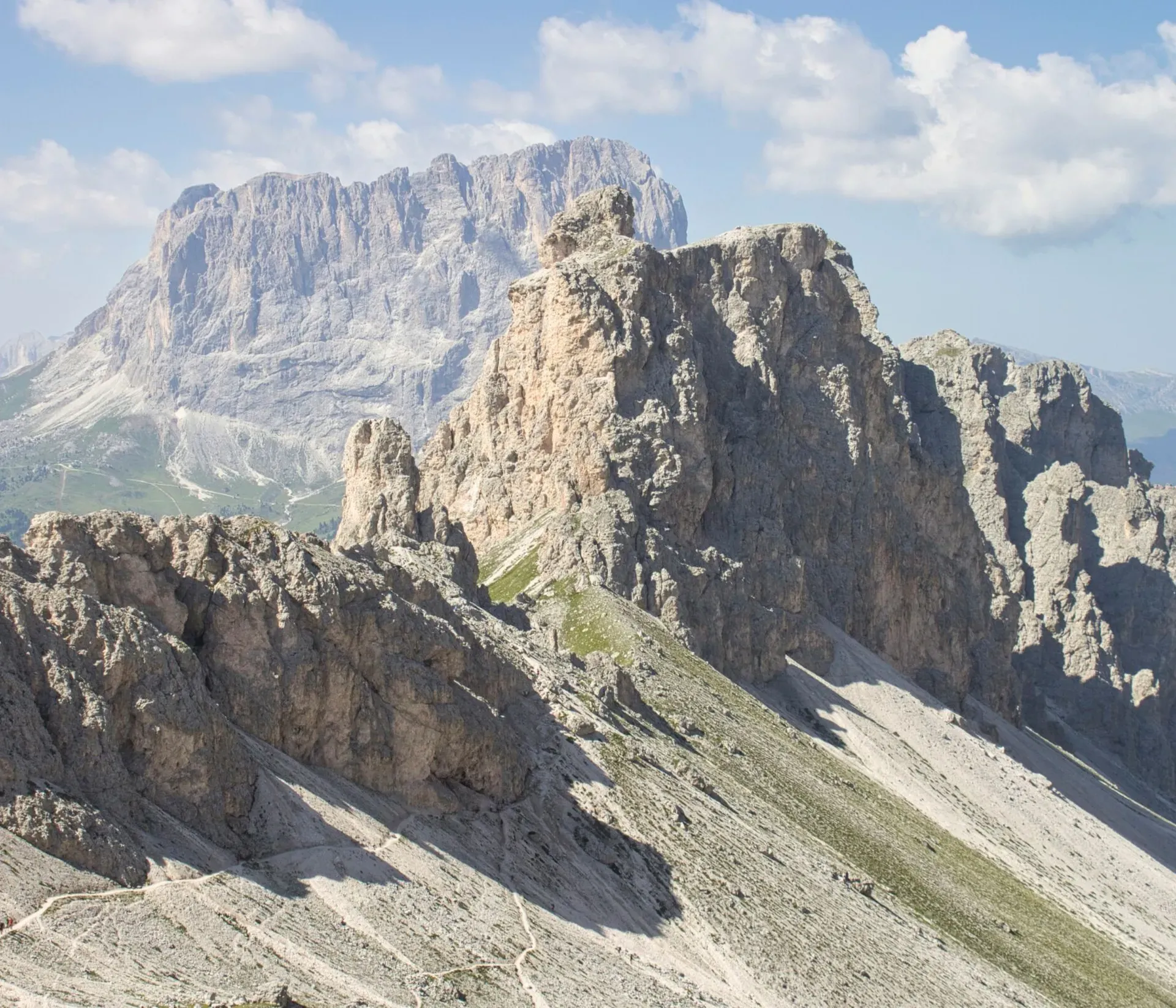 View of Forcella Cir with a trail running along the mountain ridge, and the Cir peaks and Sassolungo massif in the background.