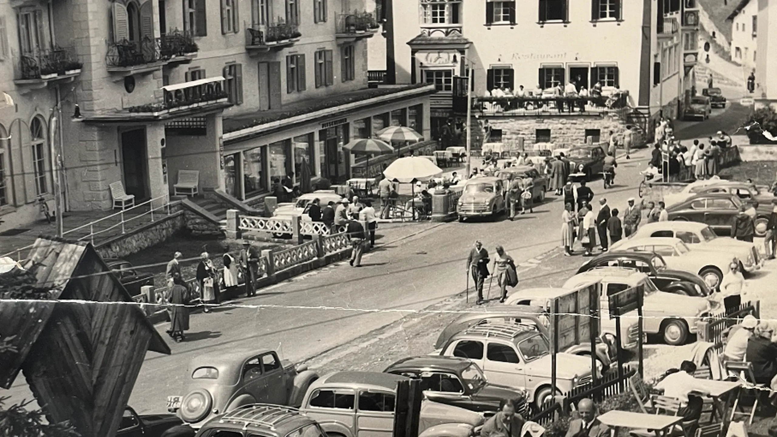 Vista della terrazza e della piazza di fronte all’Hotel Oswald, affollata di persone, sottolineando come l’hotel sia sempre stato un punto di riferimento per la comunità locale.